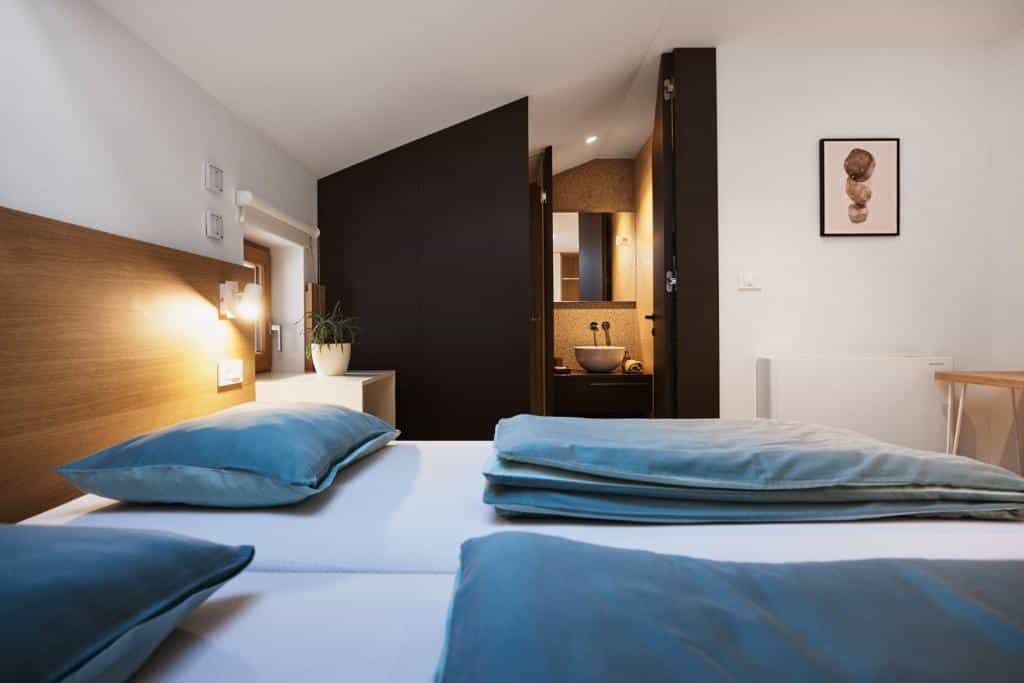 Bedroom with white walls, wooden headboard, blue pillows, and view into a modern bathroom.