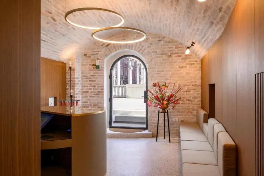 Hotel reception with exposed brick, modern lighting, and view through arched doorway to columns.