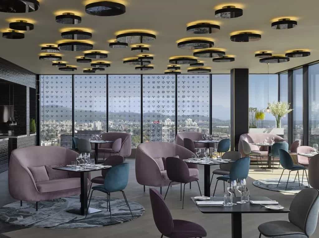 Modern restaurant dining area with velvet seating and city view through large windows