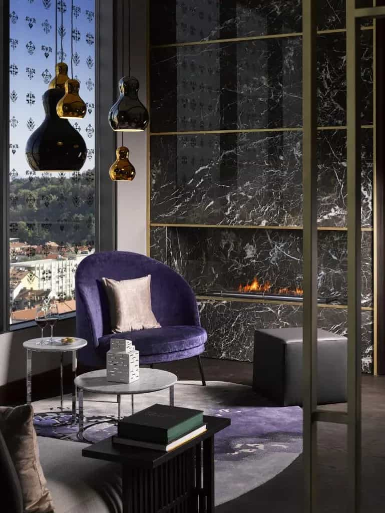 Luxury lounge with purple chair, modern lighting, and black marble fireplace overlooking a city view.