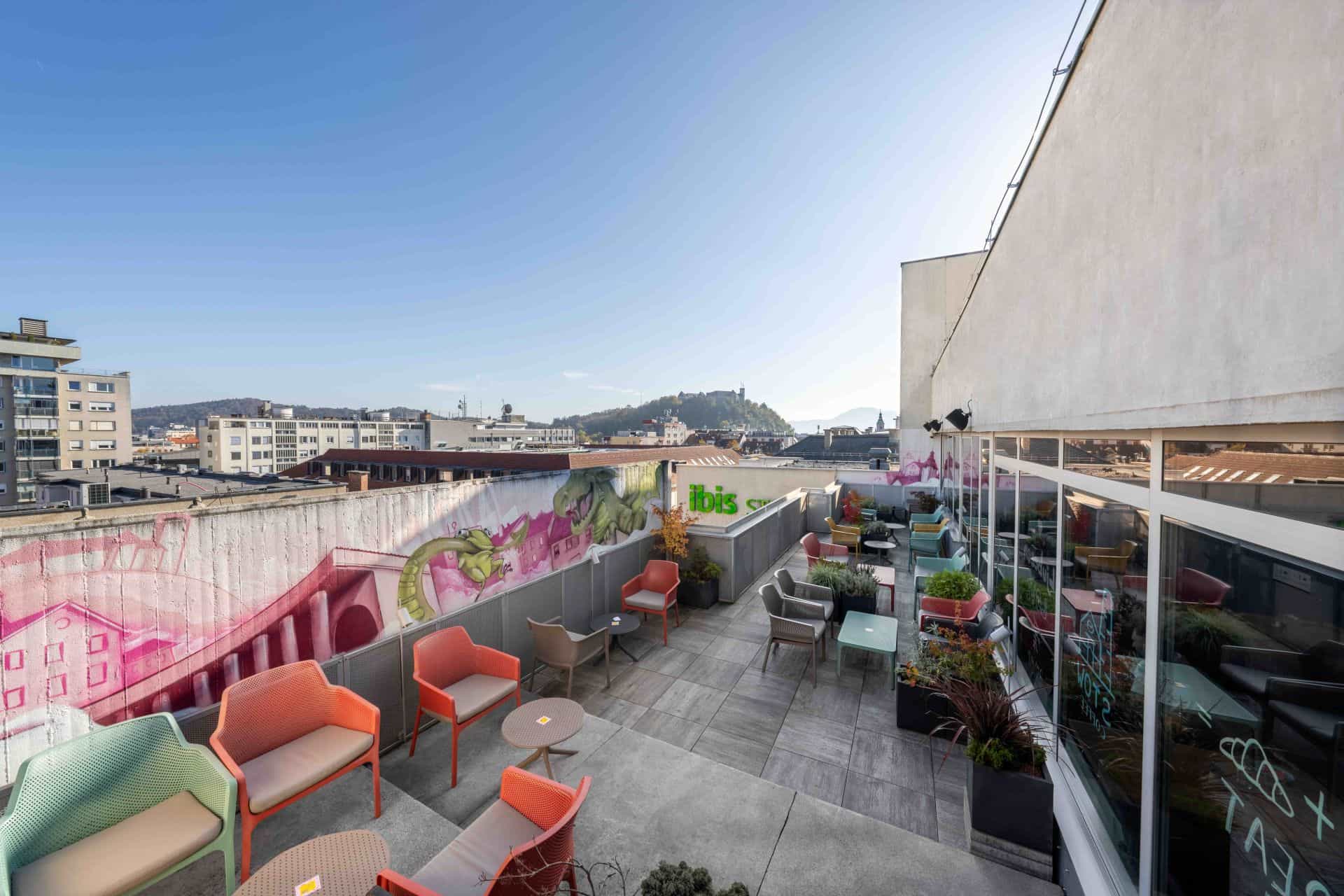 Rooftop terrace with colorful chairs and city view including Ljubljana Castle on hill