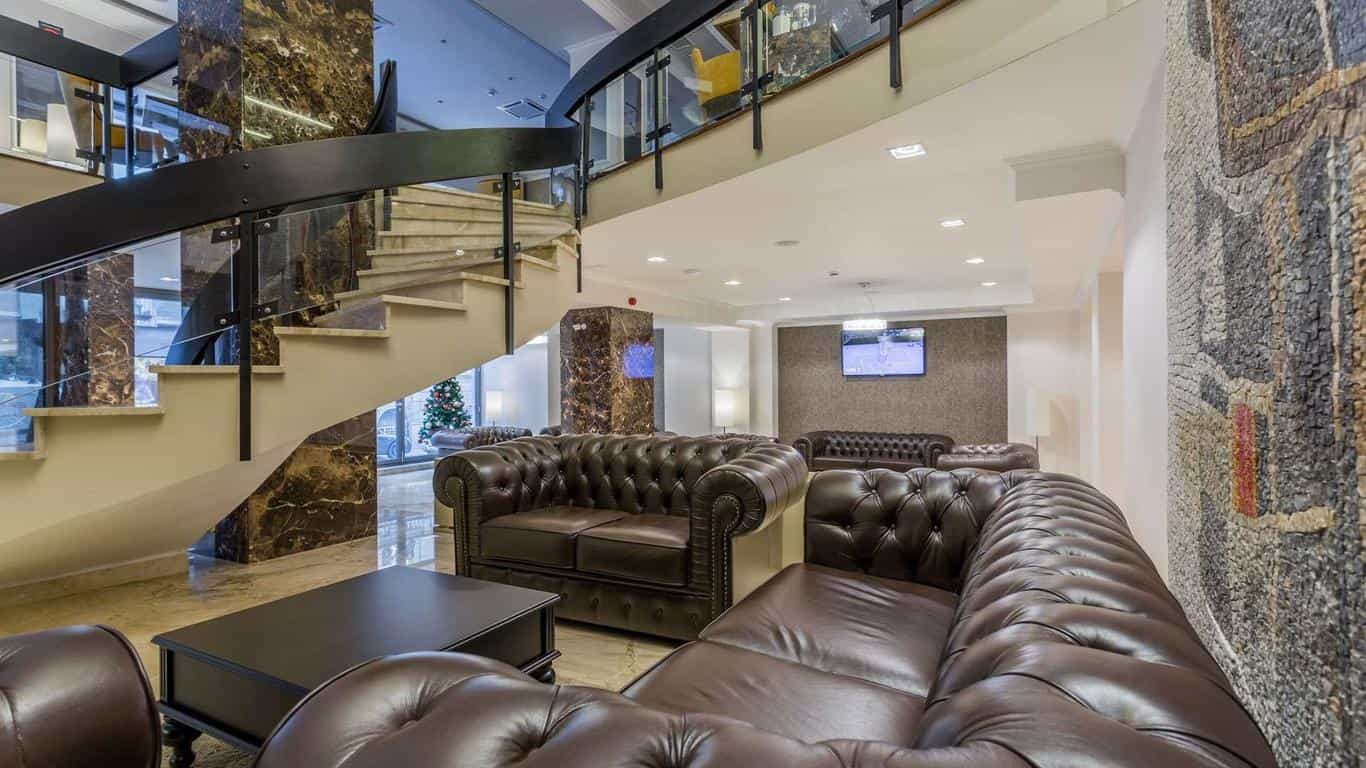 Lobby with curved staircase, brown leather Chesterfield sofas, and mosaic wall art, Royal Inn Beograd.