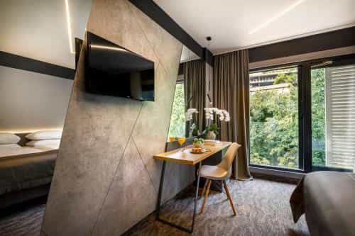 Modern hotel room with desk, TV, and view of lush green trees outside window