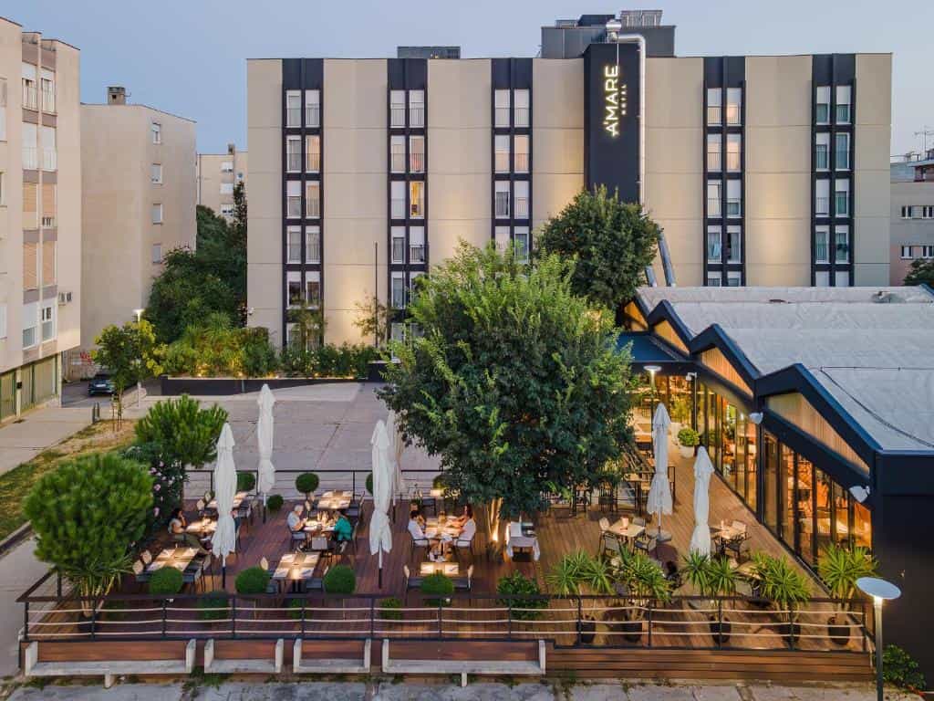 Outdoor dining terrace with tables and umbrellas in front of the Amare Hotel building