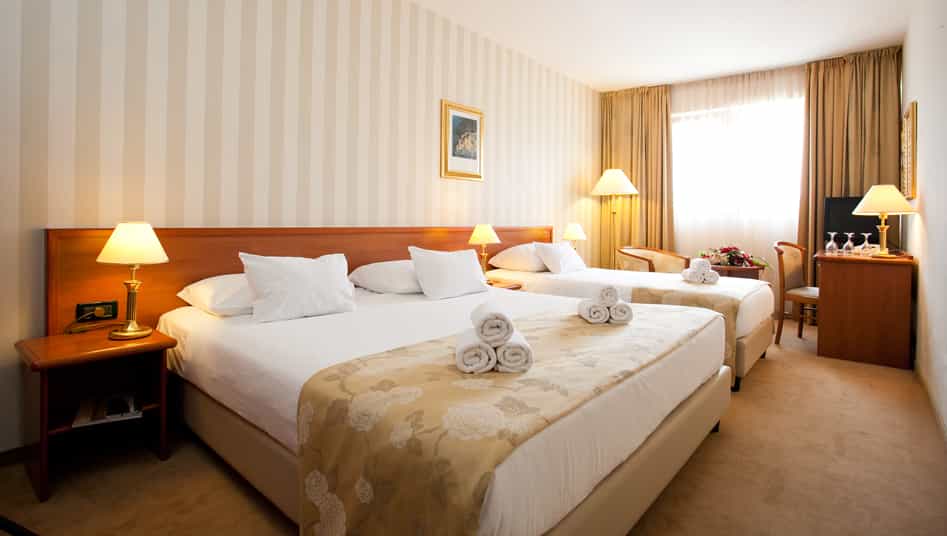 Hotel room with two beds, white linens, rolled towels, and striped wallpaper