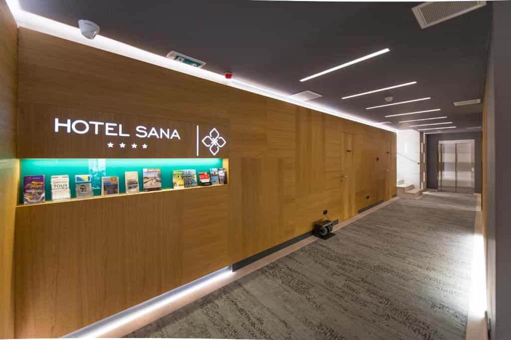 Hotel Sana lobby hallway with illuminated signage, wood paneling, and elevator access.