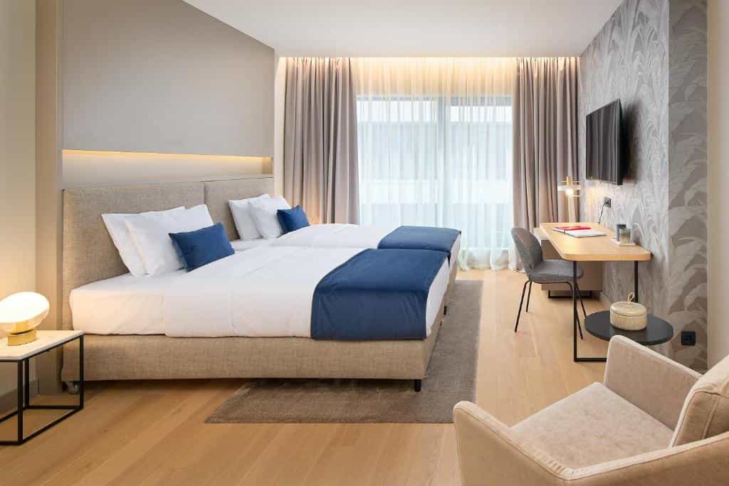 Twin beds with white linens and blue accents in a modern hotel room with wood floors.