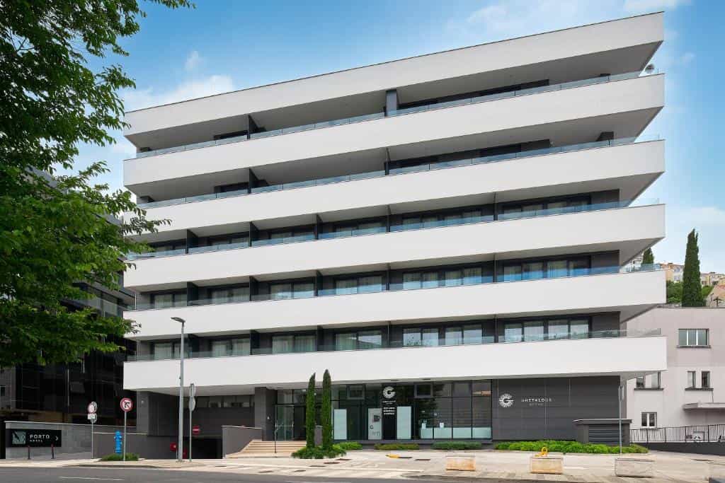 Modern white apartment building with stacked balconies and green trees on a sunny day.