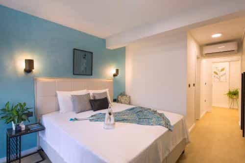 Hotel bedroom with white bedding, blue accent wall, and hallway leading to an air conditioning unit.