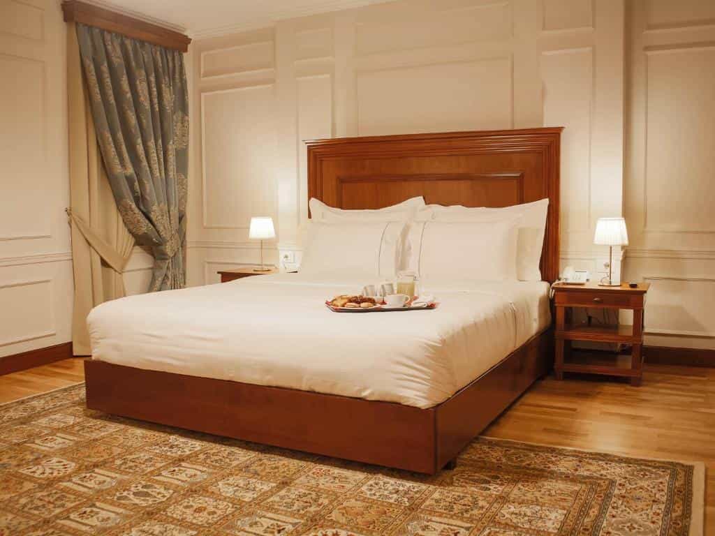 Hotel bedroom with large bed, white linens, wooden headboard, and breakfast tray.