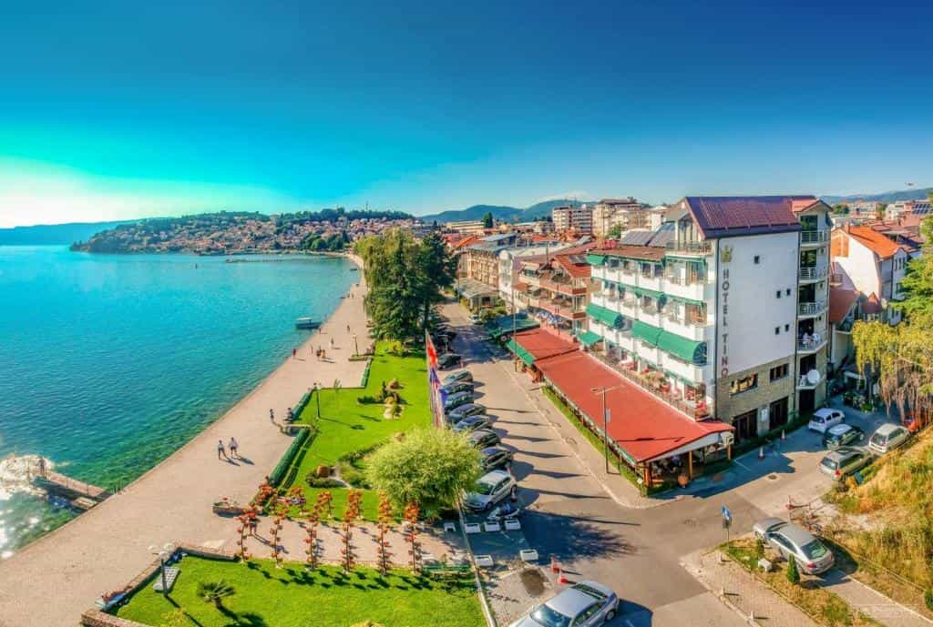 Hotel Tino on Lake Ohrid waterfront with green park and town buildings under clear blue sky.