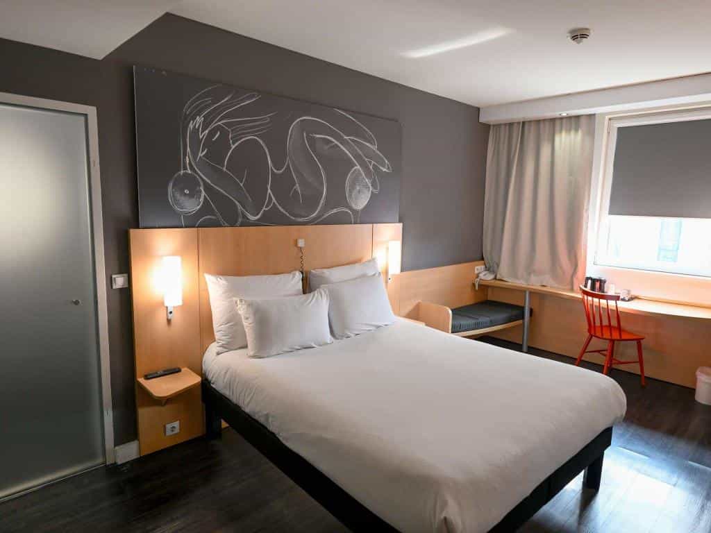 Hotel room with white bedding, dark wood floor, and large chalk-style artwork above the headboard.