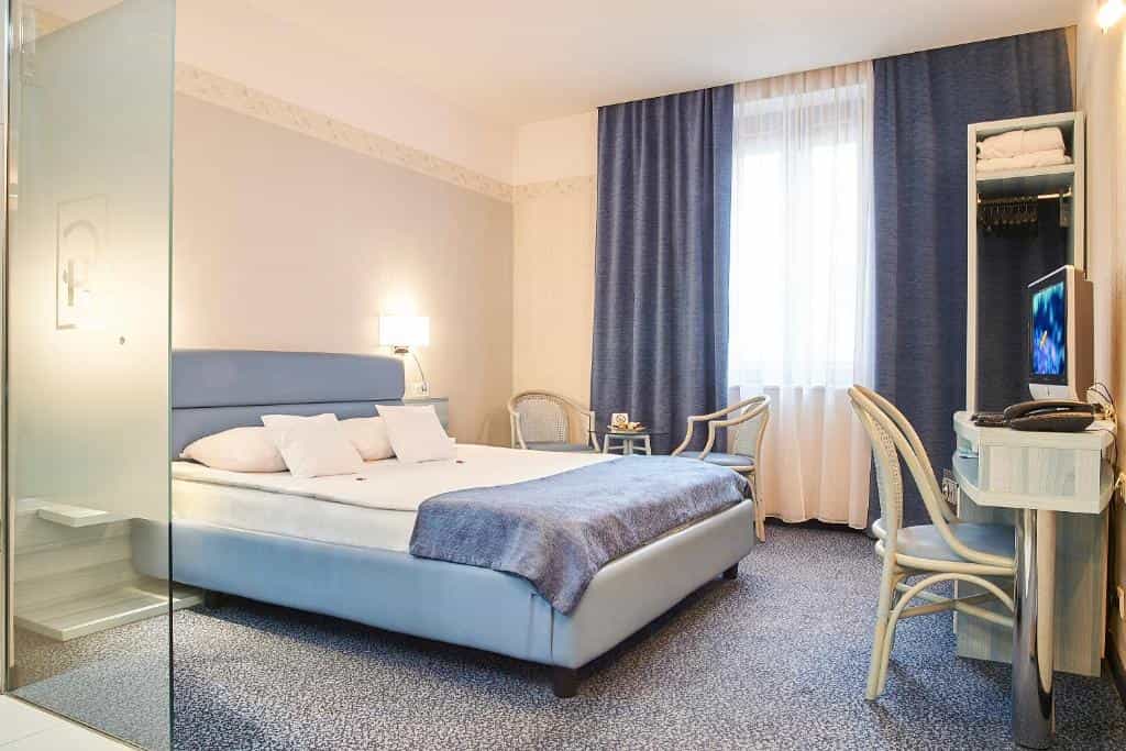 Hotel bedroom with blue bed, desk, and window with blue curtains in Sibiu.