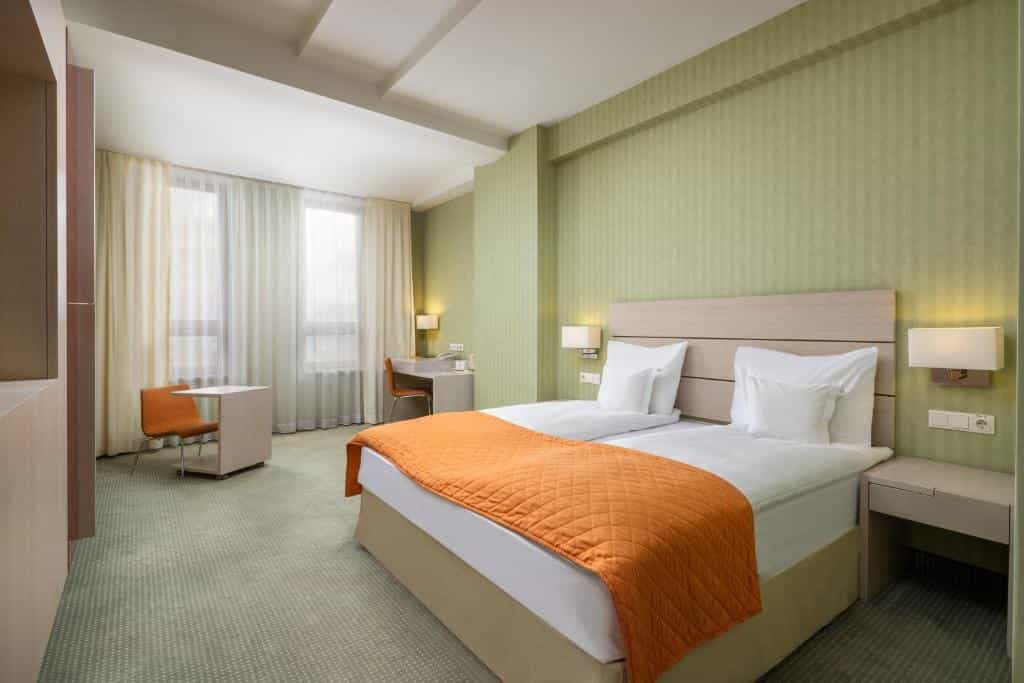 Twin beds with white linens and orange throw in hotel room with green striped walls