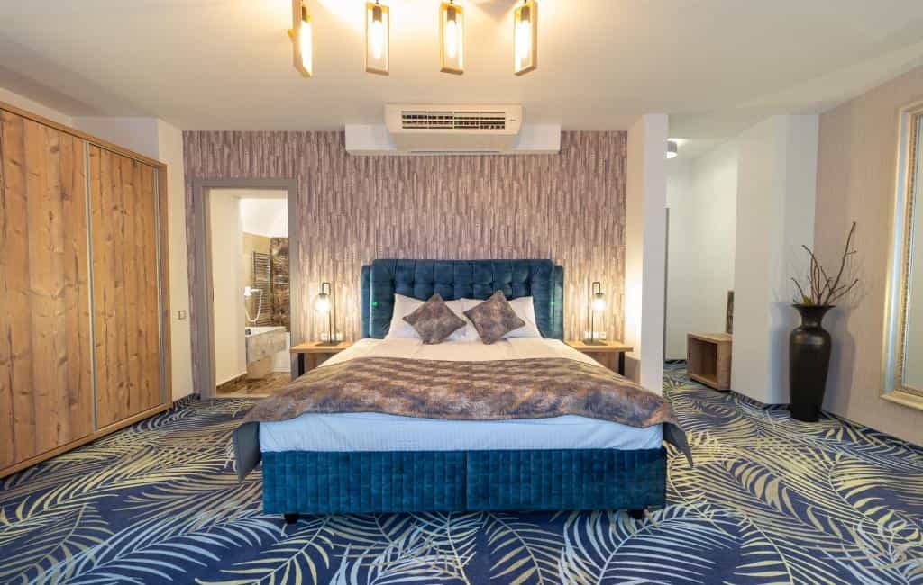 Hotel room with teal upholstered bed, patterned carpet, and wooden wardrobe, Sibu.