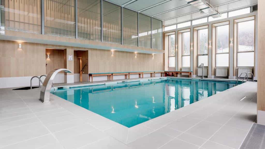 Indoor swimming pool with a stainless steel waterfall feature and large windows showing a misty outdoor scene.