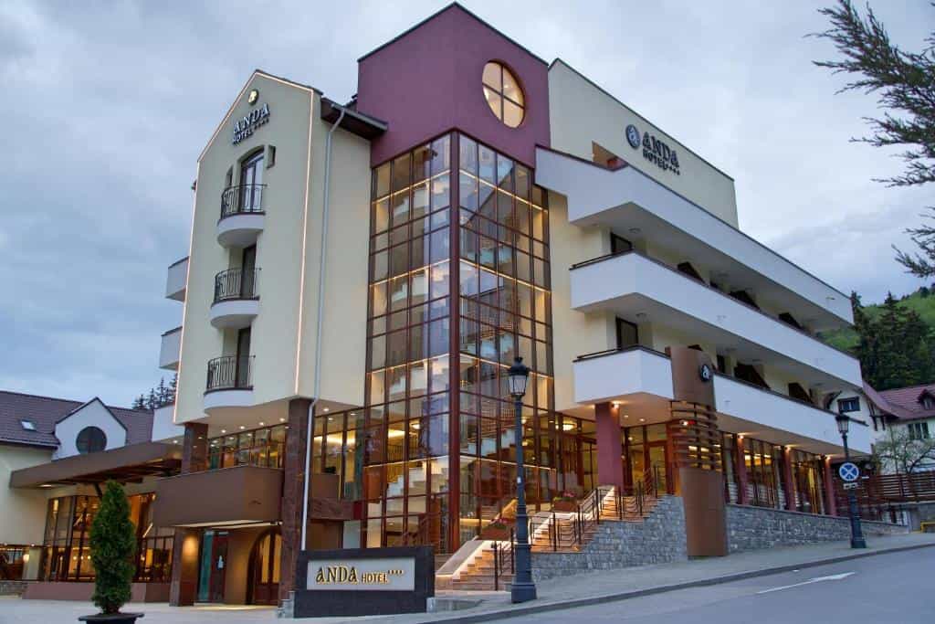 Anda Hotel building with modern glass facade and balconies in a mountainous setting.