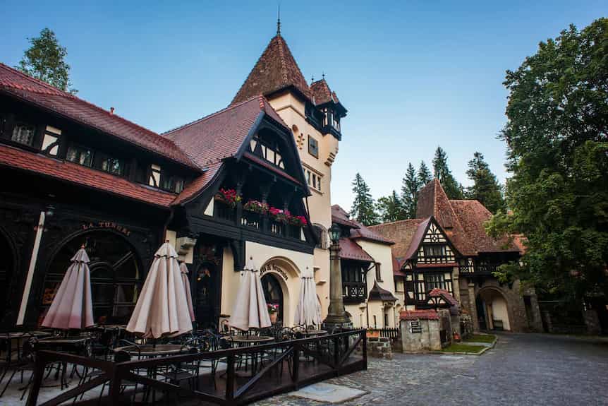 Tudor-style building with outdoor cafe seating and closed umbrellas near forest trees.
