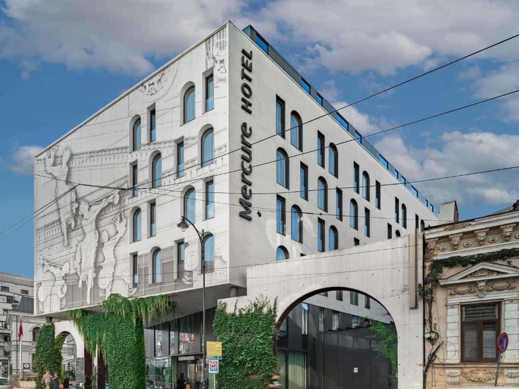 Mercure Hotel Bucharest City Center building with arched windows and large mural under blue sky.