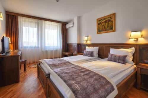 Twin hotel room with wooden furniture, white bedding, and large window with sheer curtains