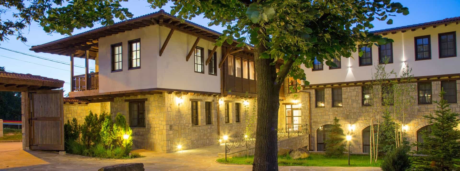 Stone and white stucco hotel exterior with wooden balconies illuminated at dusk, Arbanaski Han.