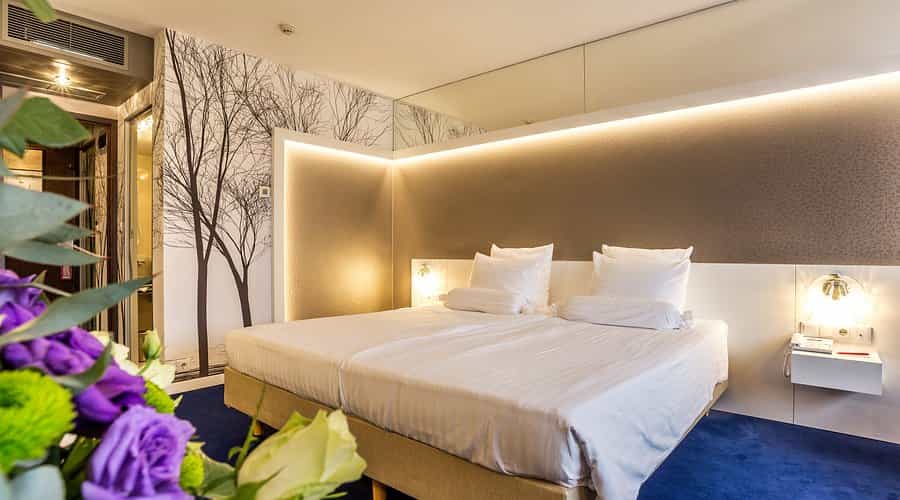 Twin beds with white linens in a modern hotel room featuring tree mural and accent lighting.