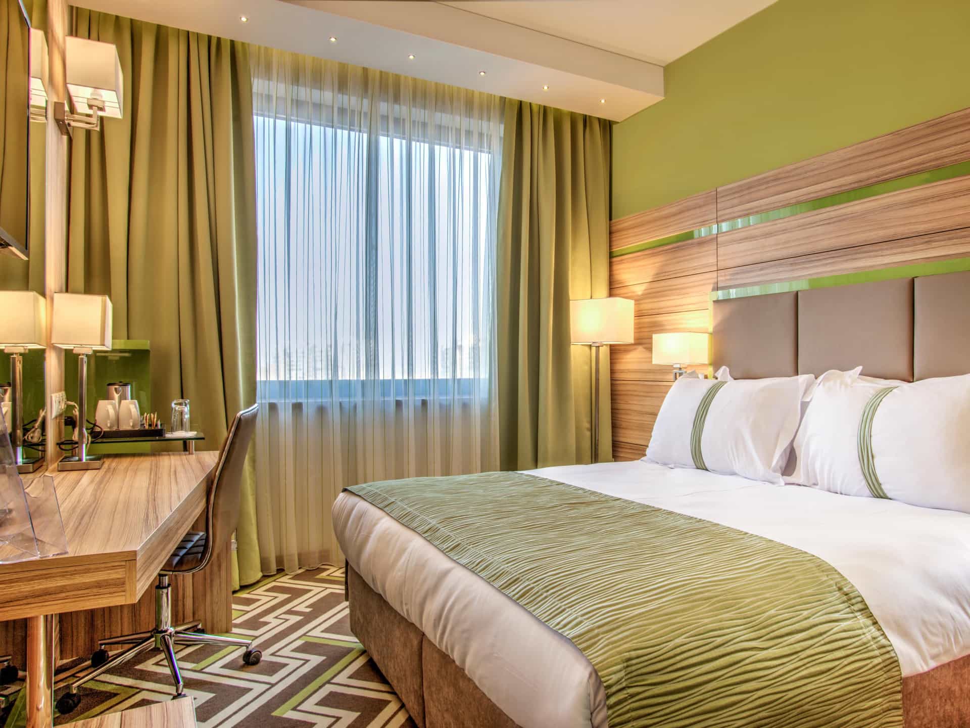 Hotel room with green walls, wood accents, white bedding, and a window with sheer curtains.