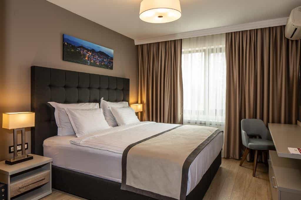 Hotel bedroom with large bed, dark headboard, bedside lamps, and city view artwork above.