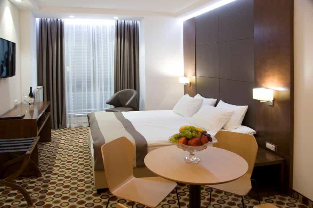 Hotel room with large bed, fruit bowl on table, and window with dark curtains in Central Sofia.