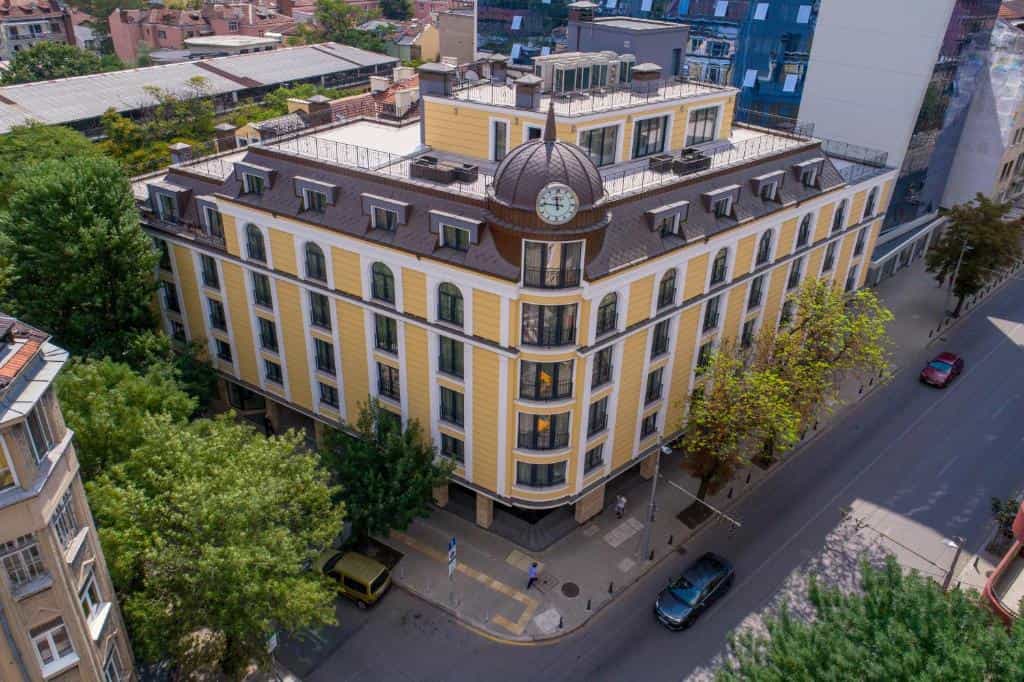 Yellow hotel building with clock tower corner in city setting, Sofia, Bulgaria.