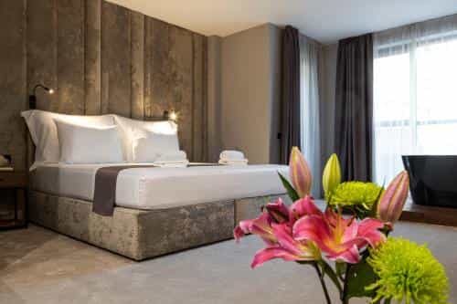 Hotel room with large bed, textured headboard, and flowers in foreground near a black tub.