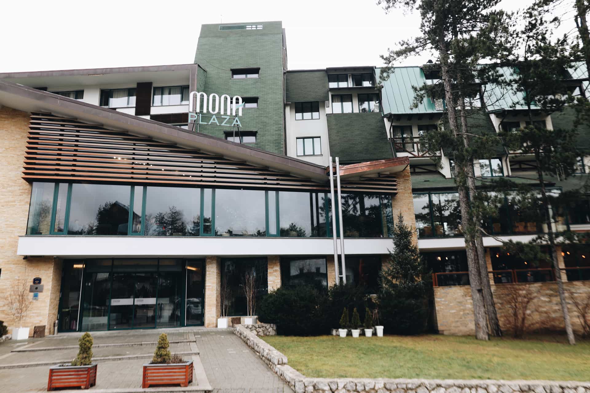 Mona Plaza hotel exterior with green roof sections and surrounding pine trees in Zlatibor.