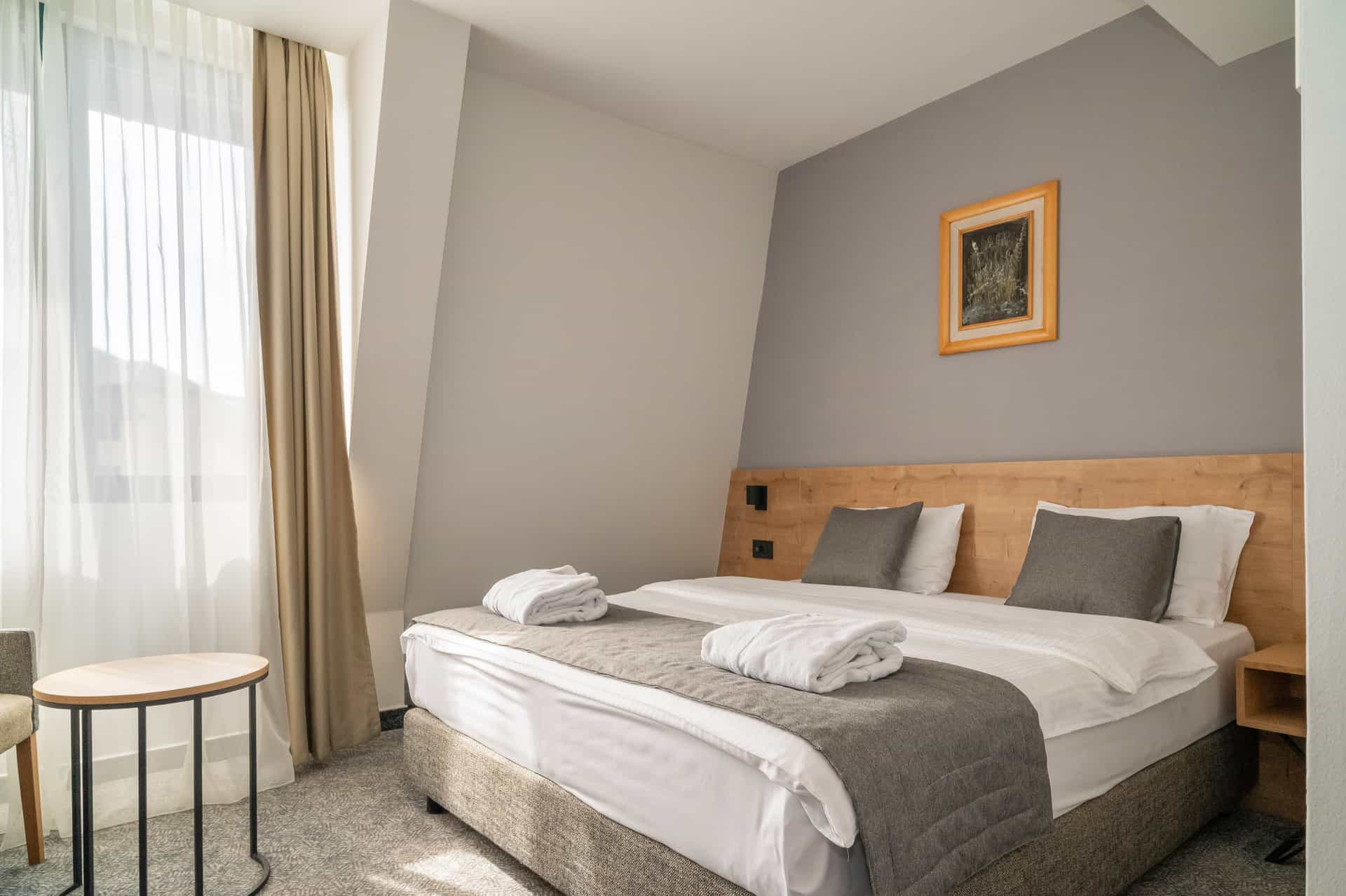 Hotel room with made bed, white linens, and window light in Mona Plaza Zlatibor.