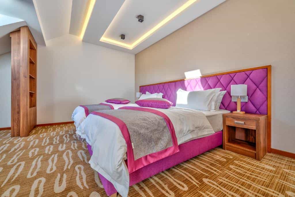 Twin hotel room with bright magenta beds, white linens, and modern recessed ceiling lighting in Buket Hotel Zlatibor.