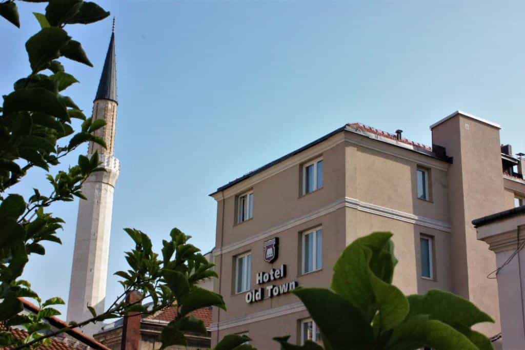 Hotel Old Town Sarajevo building facade next to a white minaret under blue sky.