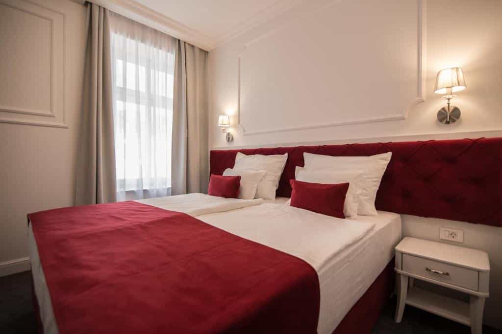 Hotel room with twin beds, white linens, red accents, and sheer window curtains.
