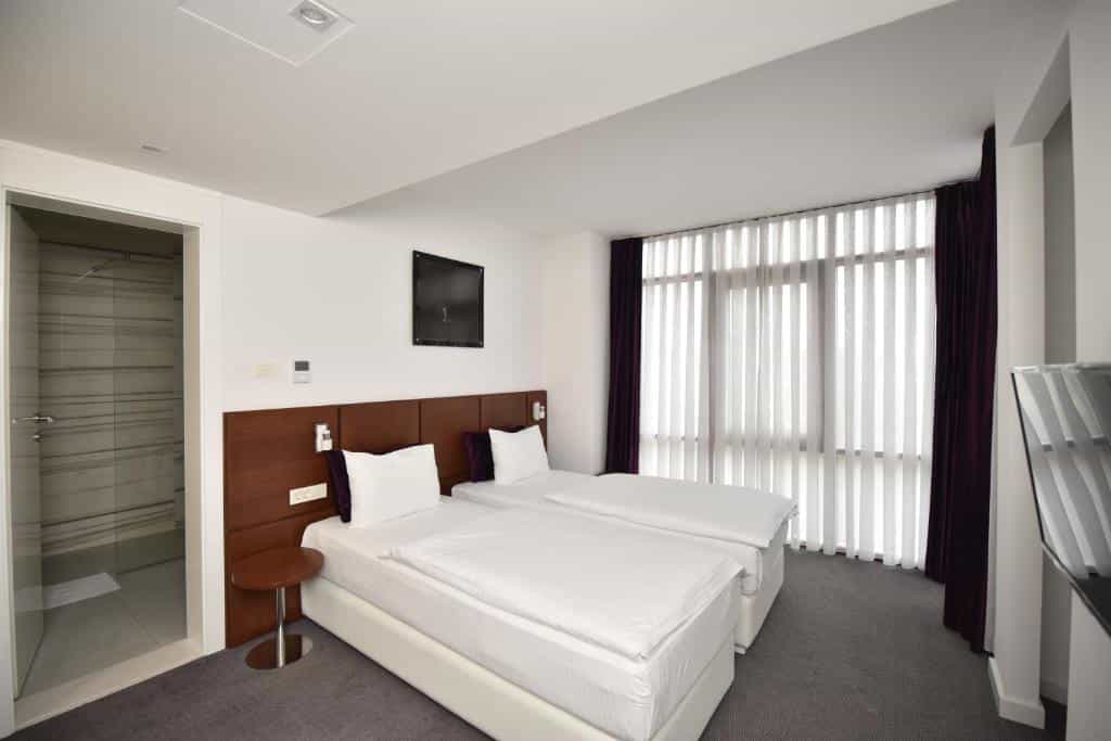 Twin beds with white linens in a modern hotel room next to a glass shower stall.