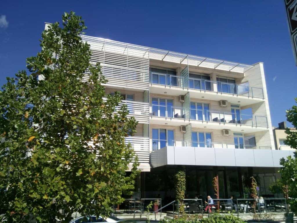 Modern hotel building with balconies, large tree, and outdoor cafe seating in Trebinje.