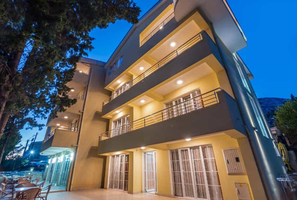 Illuminated yellow apartment building exterior with balconies and outdoor seating area at dusk
