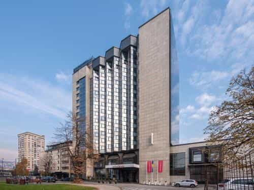 Movenpick Hotel Sarajevo exterior with modern facade, stone cladding, and blue sky.