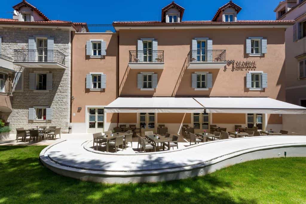 Hotel Marul exterior with outdoor dining patio, stone accents, and green lawn under blue sky.