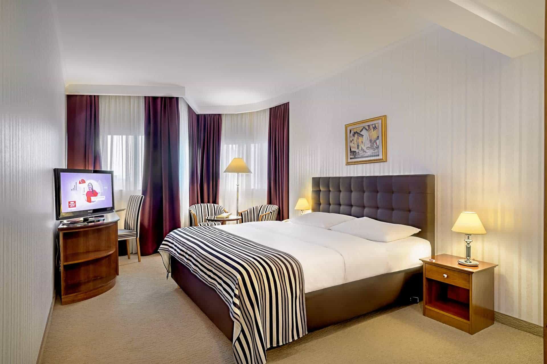 Hotel bedroom with large bed, television, and dark purple curtains near window