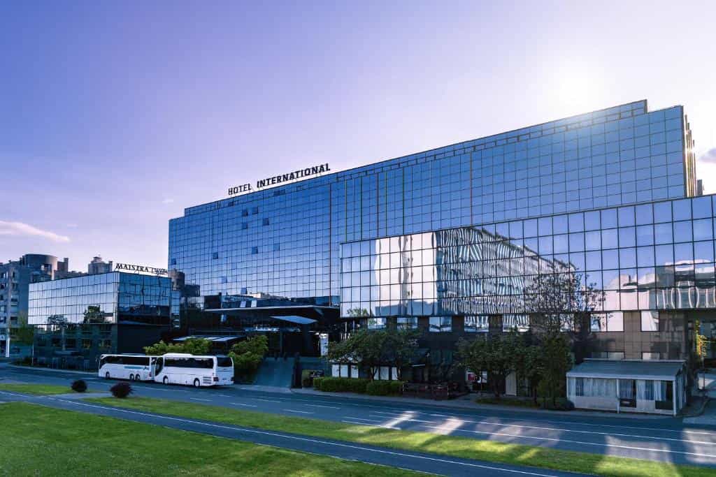 Hotel International building with glass facade, buses parked outside on a sunny day.