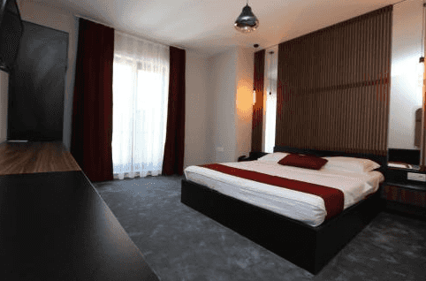 Modern hotel bedroom with white bedding, red accents, and dark wood headboard paneling