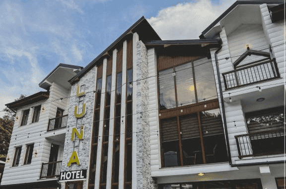 Hotel Luna Prizren exterior with white siding, stone accents, and large windows under a cloudy sky.