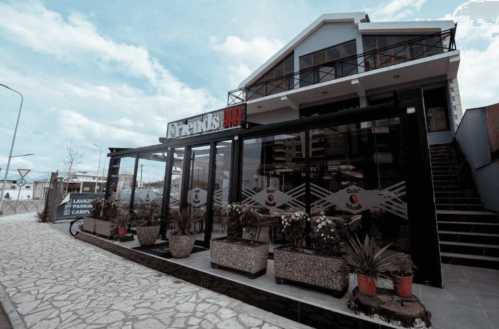 Friends Bar building with glass facade, potted plants, and stone walkway under cloudy sky