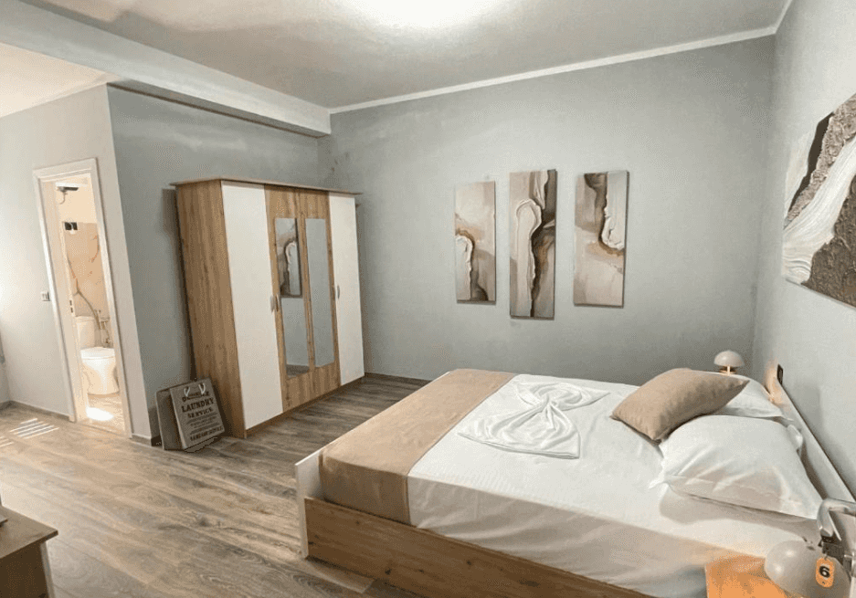 Bedroom with wooden floor, modern wardrobe, abstract art, and view into a bathroom.