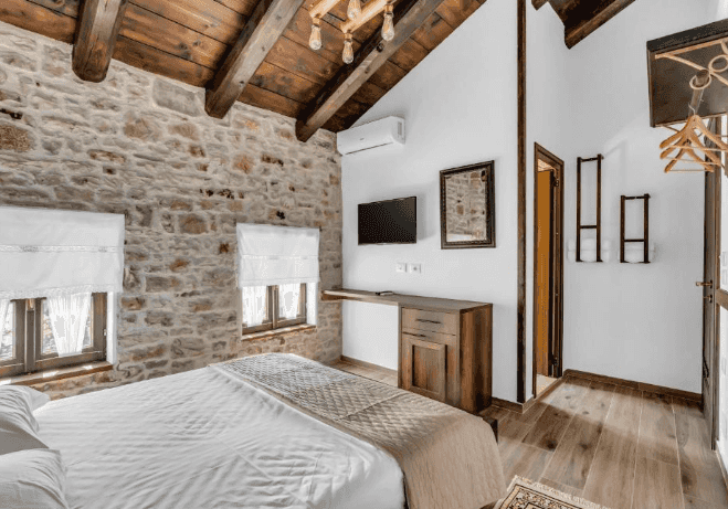 Hotel room with stone wall, wood beams, white bedding, and dark wood furniture in Berat.