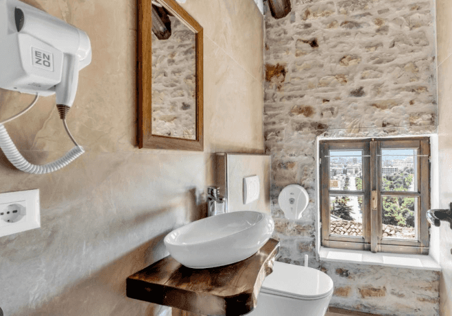Bathroom with stone walls, vessel sink on wood vanity, and view of Berat city from window.