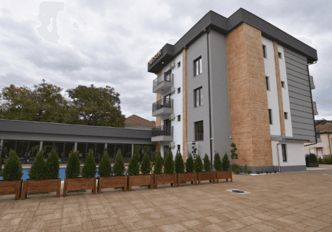 Hotel Vittore exterior with modern gray and brown facade, outdoor pool area, and potted evergreens.
